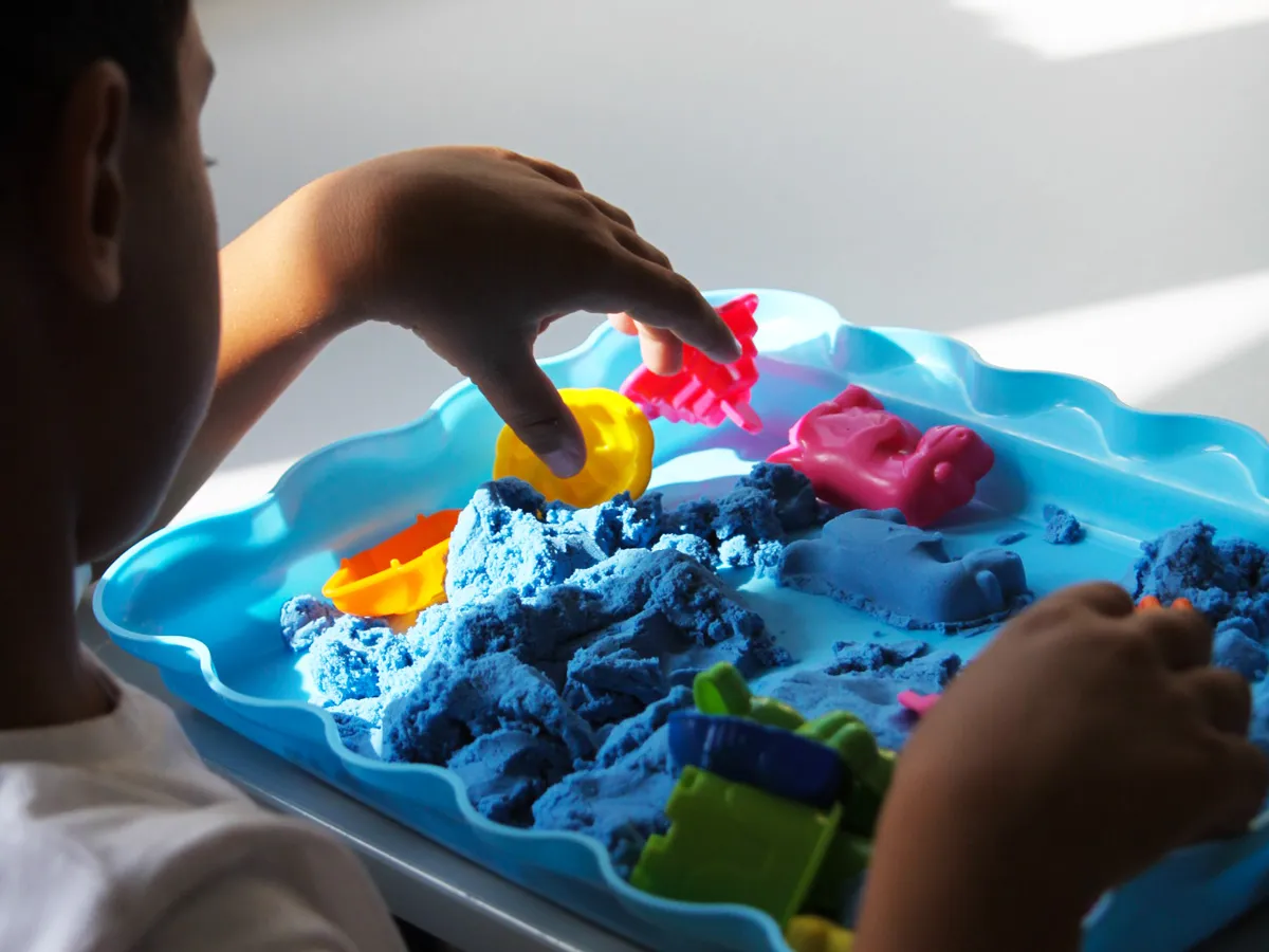 Enfant manipulant du sable sensoriel et des formes colorées au DAPE